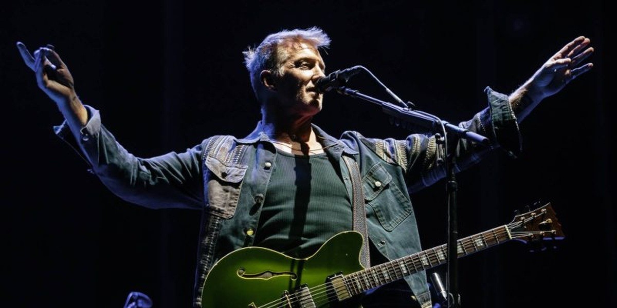 Josh Homme on stage with a guitar and his arms outstretched